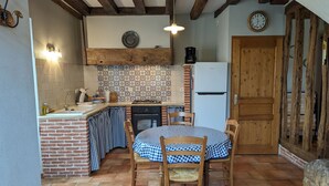 A rustic kitchen with a brick backsplash, a wooden table with checkered tablecloth, and a wooden door. - Charming 17th-Century Country House with Garden, BBQ, Terrace, and Ping-Pong Near Fontainebleau (Lorcy)