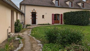 A two-story house with a tiled roof, a front door with a small window, and a garden with a hedge and plants. - Charming 17th-Century Country House with Garden, BBQ, Terrace, and Ping-Pong Near Fontainebleau (Lorcy)
