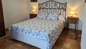 A neatly made bed with floral bedding, two bedside tables with lamps, and a painting on the wall. - Charming 17th-Century Country House with Garden, BBQ, Terrace, and Ping-Pong Near Fontainebleau (Lorcy)