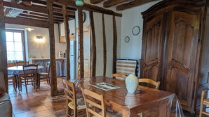 A rustic dining area with a wooden table and chairs, a vase on the table, and a kitchen in the background. - Charming 17th-Century Country House with Garden, BBQ, Terrace, and Ping-Pong Near Fontainebleau (Lorcy)