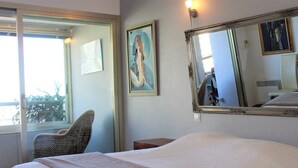 A hotel room with a large bed, a chair, a painting, and a mirror.