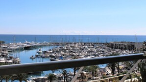 A marina with numerous boats docked, a clear blue sky, and a view of the sea.
