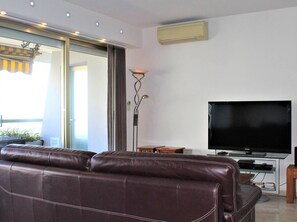 Sala de estar com sofá de couro marrom, televisão de tela plana em um suporte e luminária de chão.