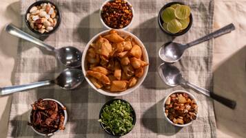Una mesa con un bol de aperitivos fritos, rodeada de pequeños recipientes con diferentes salsas y guarniciones.