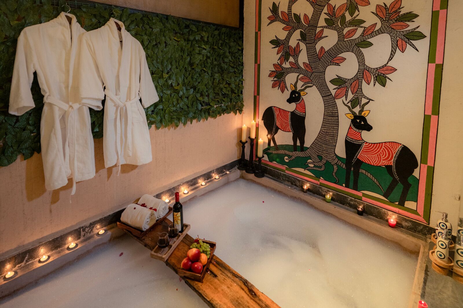 Un cuarto de spa con una bañera grande, un mural en la pared y una bandeja de madera con frutas y una botella.