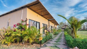 A modern building with a checkered pathway leading to the entrance, surrounded by lush greenery and flowering plants. - Panarpani Retreat Pachmarhi (Pipariya)