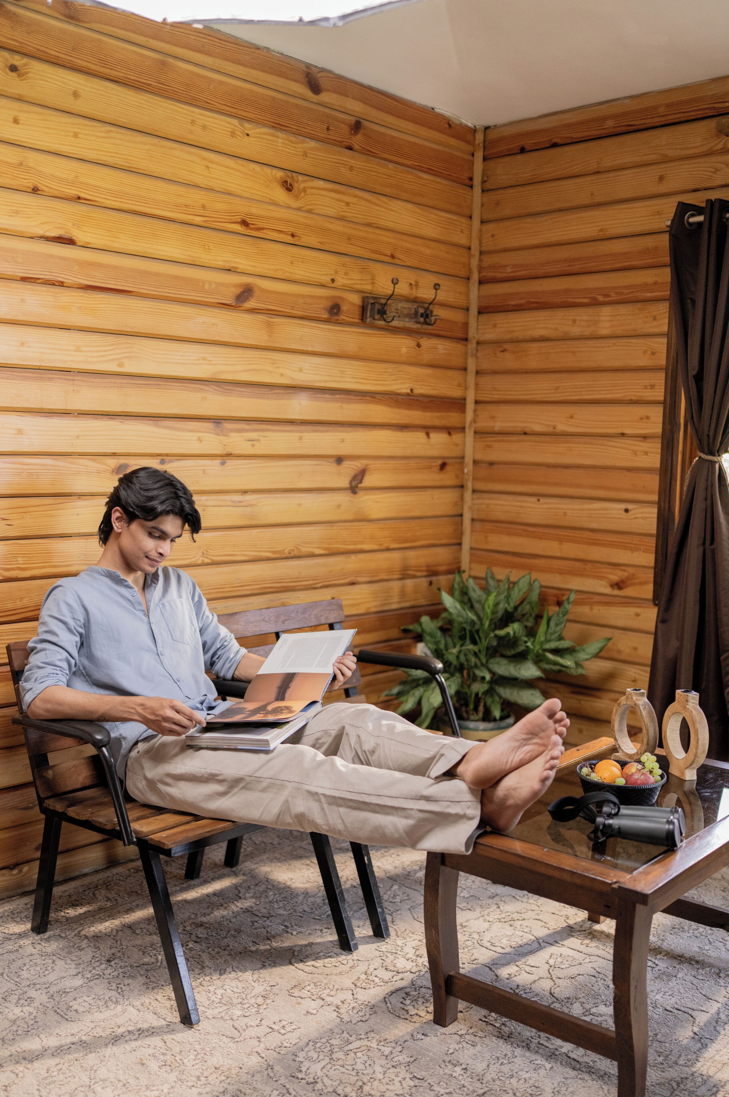 A person sitting on a wooden bench in a room with wooden walls, reading a book.