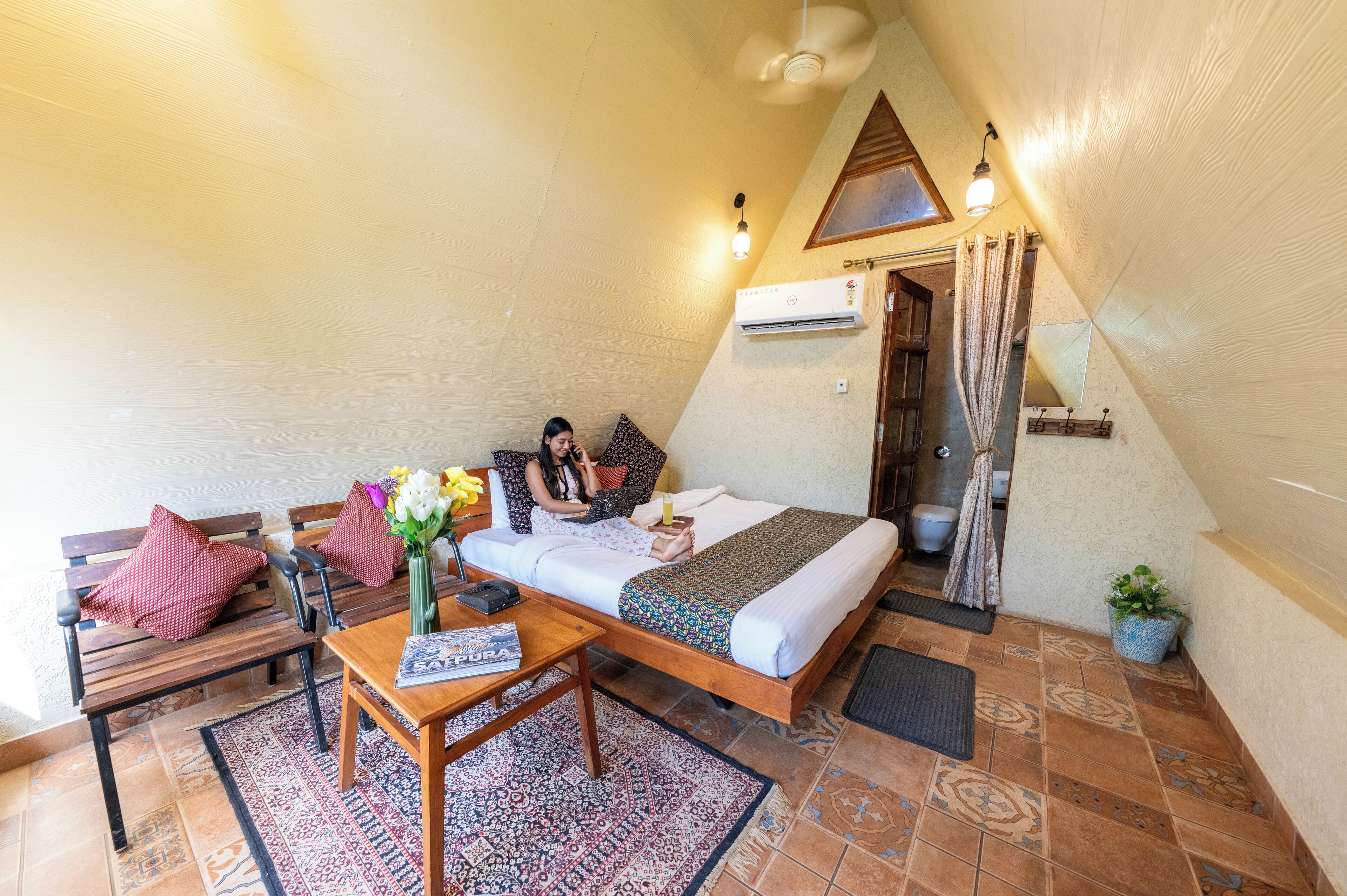 A cozy room with a bed, a wooden bench, a table with a vase of flowers, and a small potted plant.