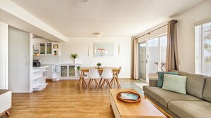 A modern living room with a wooden floor, a sofa, a coffee table, and a dining area with chairs and a table. - THE GRASSY KNOLL Panoramic Beach Apartment  - Sunrise Beach (Sunrise Beach)