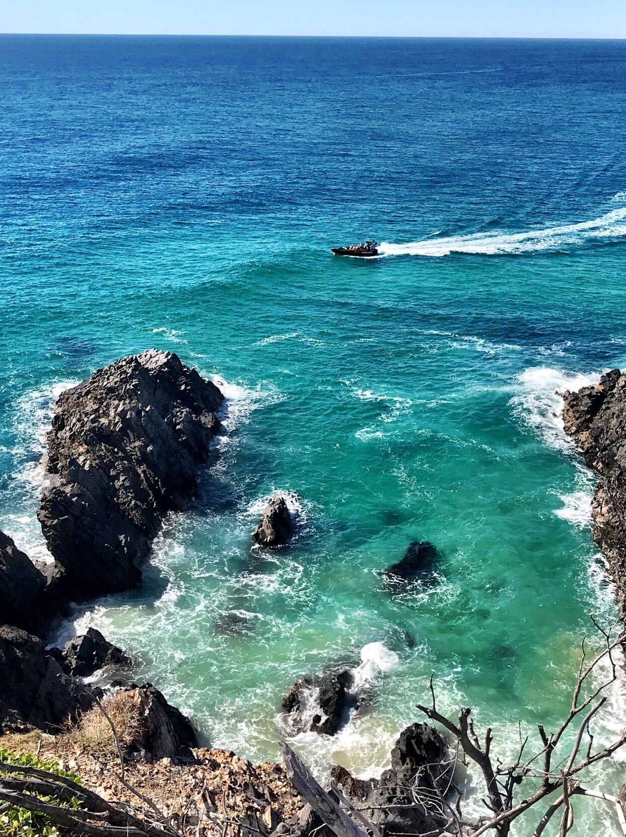 A coastal scene with clear turquoise waters, rocky outcrops, and a small boat in the distance.
