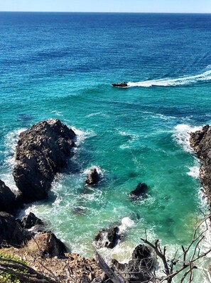 A coastal scene with clear turquoise waters, rocky outcrops, and a small boat in the distance.