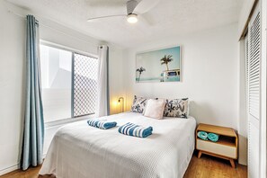 A bedroom with a bed, a nightstand, a window with curtains, a ceiling fan, and a wall-mounted painting.
