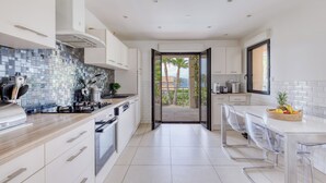 A modern kitchen with white cabinets, a tiled backsplash, and a view to an outdoor patio. - Villa at the entrance to St Tropez sea view beach 2 minutes walk (Gassin)