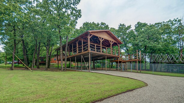 Un pavillon en bois doté d’un étage supérieur couvert, entouré d’arbres et bordé d’un chemin de gravier.