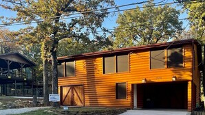 Une cabane en rondins à deux étages, dotée d’un garage, de fondations en pierre et offrant une vue dégagée sur les arbres environnants.
