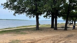 Un parc avec un sentier de terre, des tables de pique-nique et des arbres, situé près d’une étendue d’eau.
