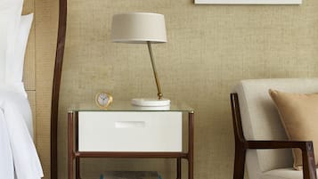 A neatly arranged bedroom with a bed, a bedside table with a lamp, a framed picture on the wall, and a chair.