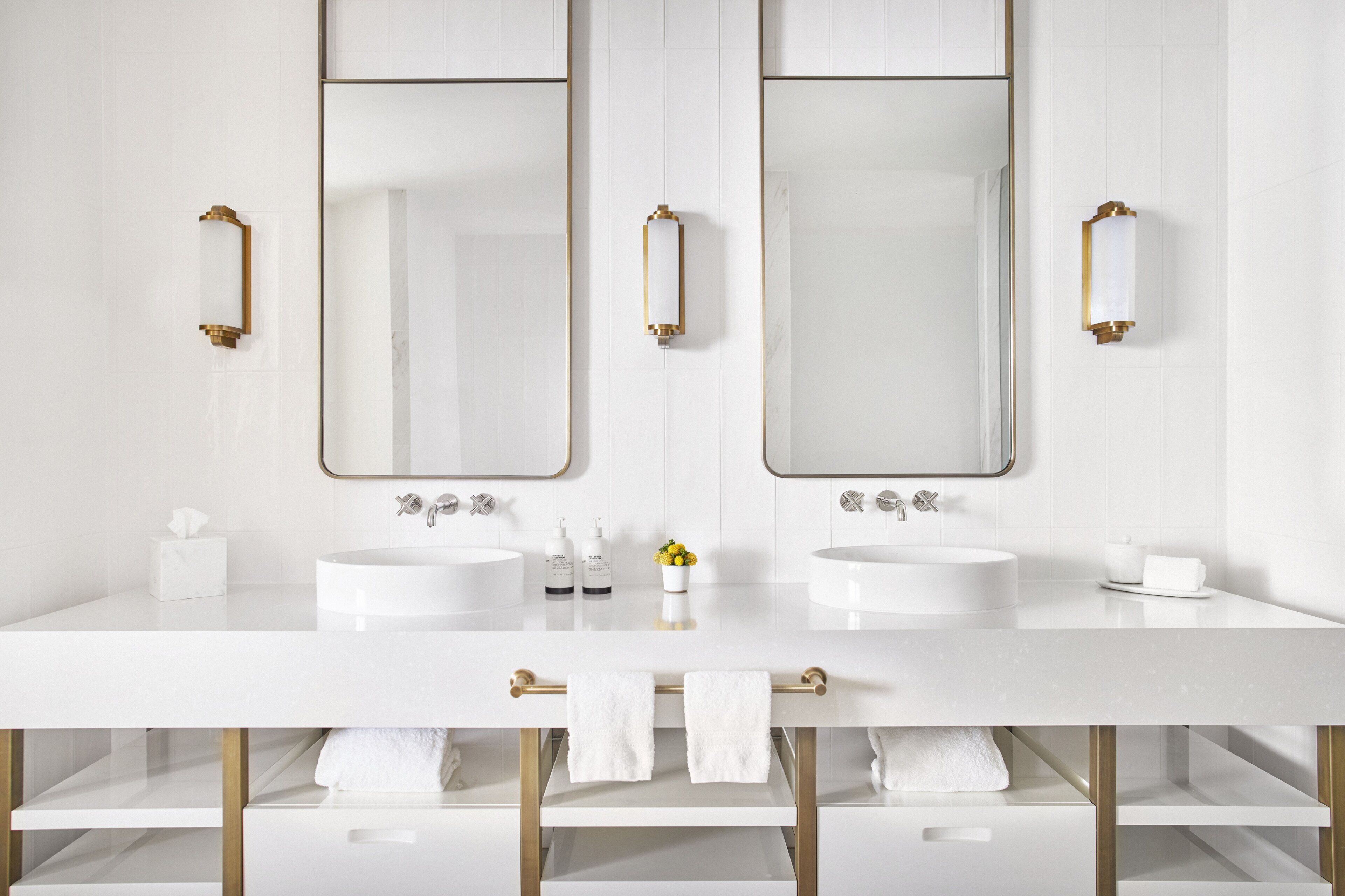 Ein modernes Badezimmer mit zwei Waschbecken, großen Spiegeln und goldenen Armaturen.