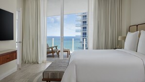 Ein Hotelzimmer mit einem großen Bett, einem Fernseher, einem Balkon mit einem Sessel und Blick aufs Meer.