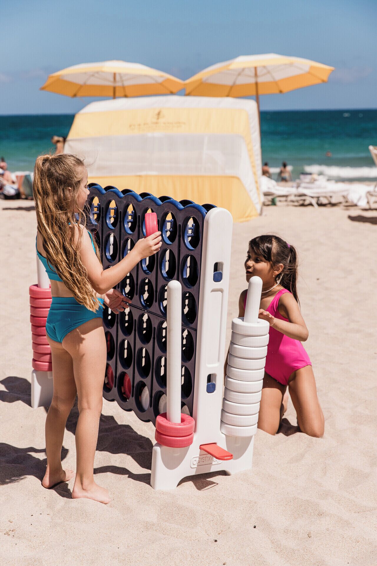 Une scène de plage avec un château de sable, des parasols et l’océan en arrière-plan.