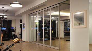 Uma academia com equipamentos de ginástica, esteira e uma porta de correr de vidro que dá para outro espaço.