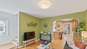 Ein Wohnzimmer mit Flachbildfernseher, Couchtisch und Sofa. Eine Treppe führt in einen anderen Raum.