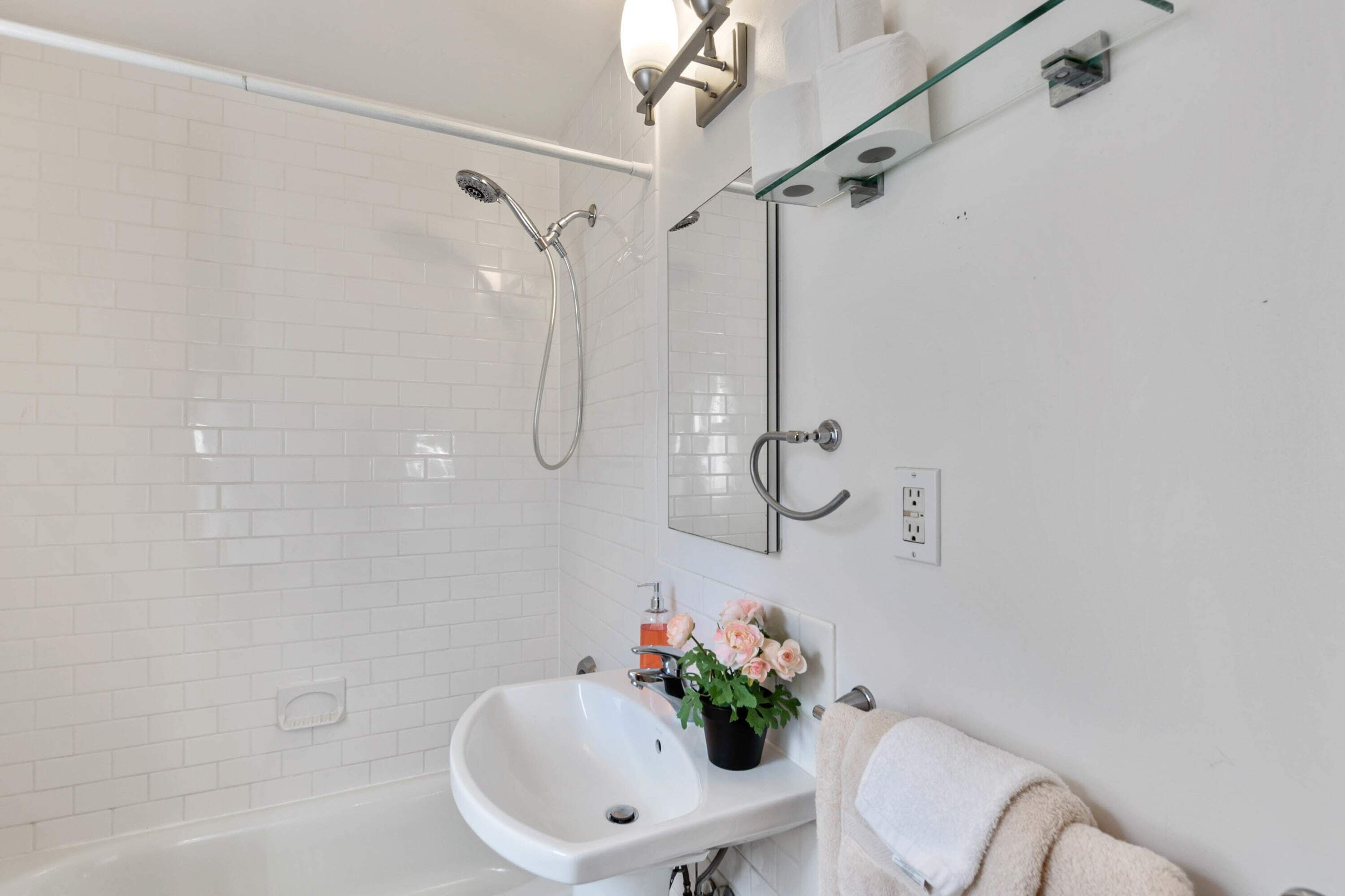 Un baño moderno con lavamanos blanco, cabina de ducha de vidrio y un espejo con toallero.