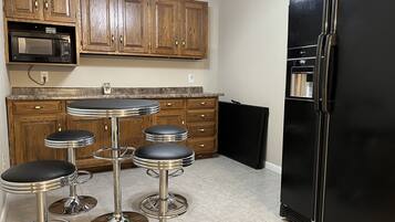 A kitchen with wooden cabinets, a black refrigerator, a microwave, and three bar stools.