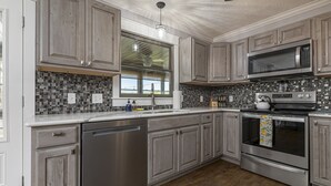 Una cocina moderna con electrodomésticos de acero inoxidable, armarios de madera, un ventanal grande y un salpicadero de azulejos.