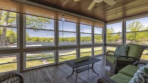 Un patio techado con mobiliario de mimbre, ventanas amplias y una mesa con un letrero.