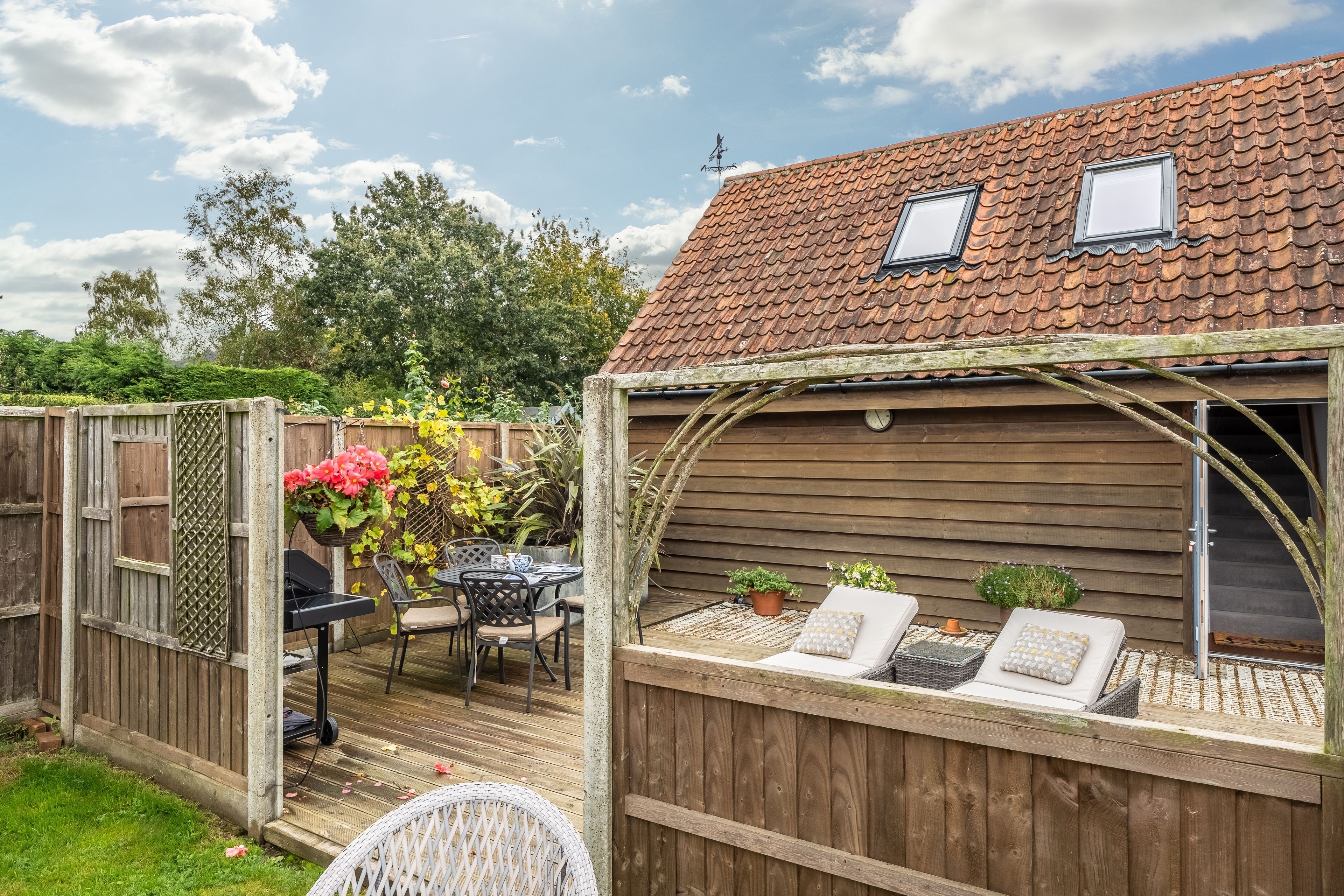 A wooden deck with outdoor furniture, a pergola, and a view of a house with a tiled roof.