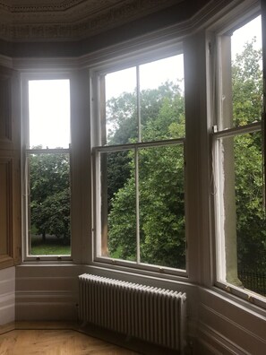 A corner room with large bay windows, a radiator, and a view of trees. - Luxurious 3-bed Apartment in Conservation Area (Glasgow)