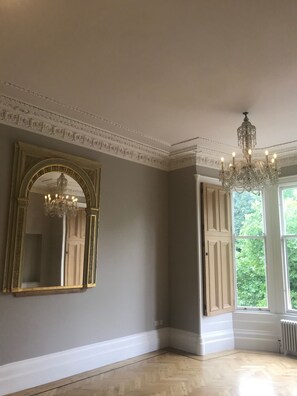 Une pièce dotée d’un grand miroir, d’un lustre et d’une fenêtre avec des volets.