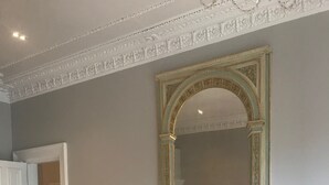 Una stanza con un pavimento in parquet a spina di pesce, un grande specchio con cornice decorata e una porta bianca.