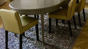 Una zona pranzo con un tavolo rotondo, sei sedie, un tappeto decorato e un mobiletto in legno con vetrate.