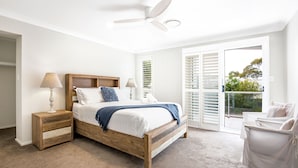 A bedroom with a wooden bed, two bedside tables, a ceiling fan, and a view of greenery outside.