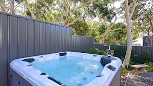 A hot tub with a waterfall feature, surrounded by a wooden fence and trees.