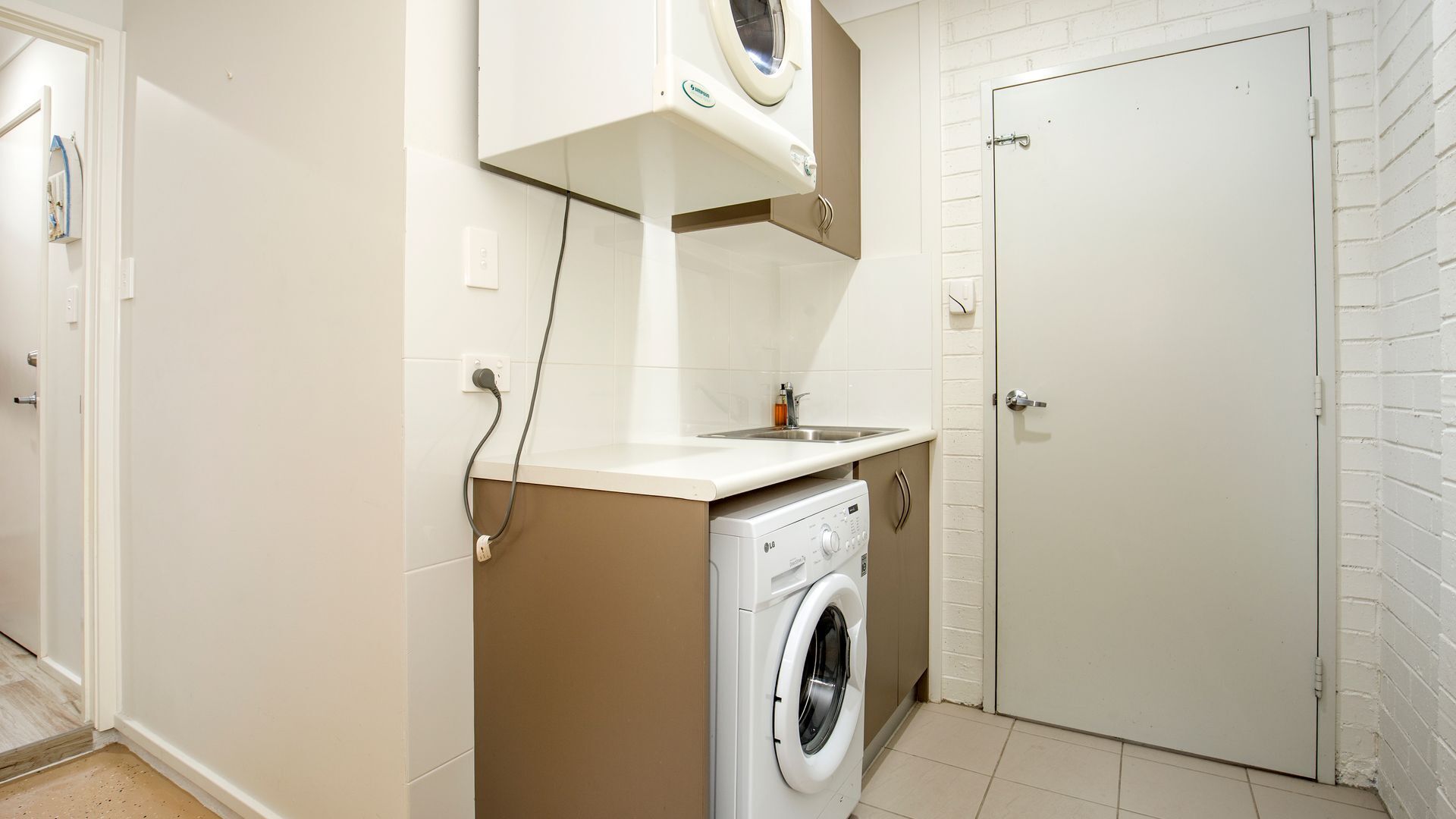 Une petite buanderie comprenant un lave-linge, un petit évier et une porte.