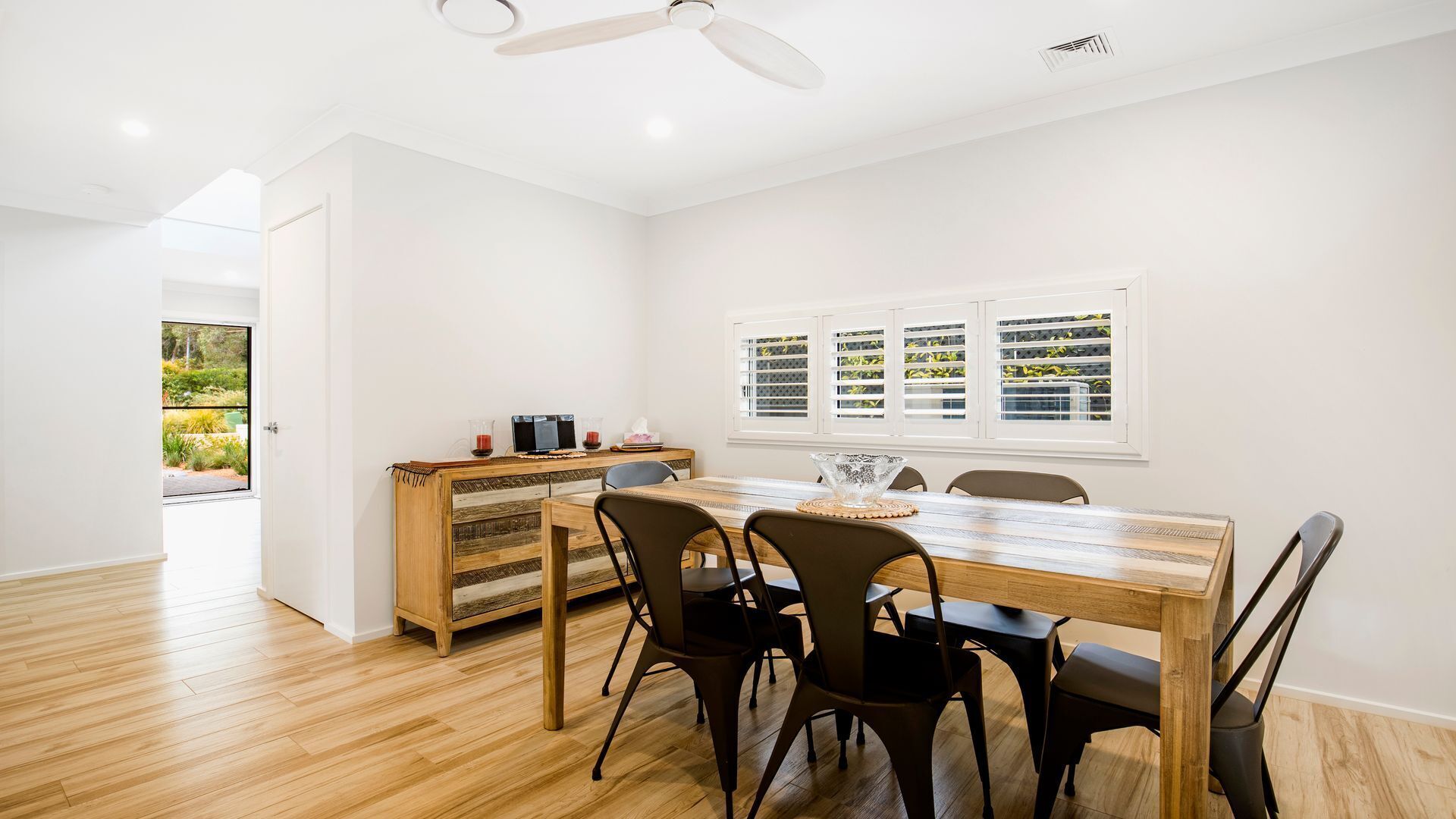 A dining area with a wooden table and chairs, a small cabinet, and a window with blinds.