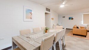Un coin repas avec une table en bois et des chaises en osier, un ventilateur de plafond et un tableau encadré au mur.