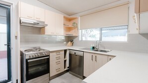 Une cuisine moderne équipée d’une cuisinière à gaz, d’un four, d’un lave-vaisselle et d’une fenêtre laissant entrer la lumière naturelle.