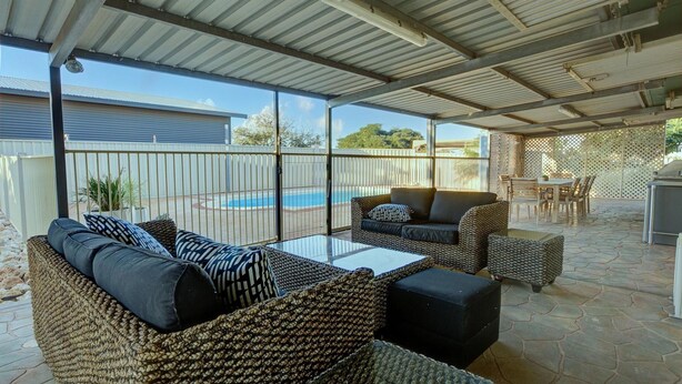 Une terrasse extérieure couverte, aménagée avec des meubles en osier, une piscine et un espace barbecue.