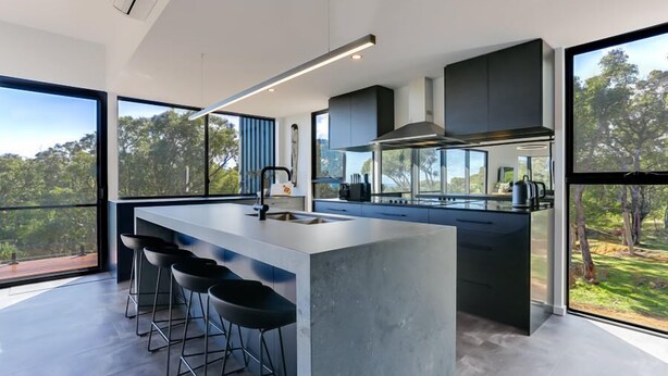 A modern kitchen with a large island, bar stools, and a view of the outdoors. - Carpe Artes – Peaceful Creative Luxury with Ocean Views (Margaret River)