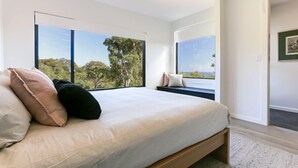 A bedroom with a large bed, a view of trees and sky through windows, and a framed picture on the wall. - Carpe Artes – Peaceful Creative Luxury with Ocean Views (Margaret River)