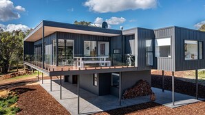 A modern, two-story house with a flat roof, large windows, and a covered outdoor area with a table and chairs. - Carpe Artes – Peaceful Creative Luxury with Ocean Views (Margaret River)