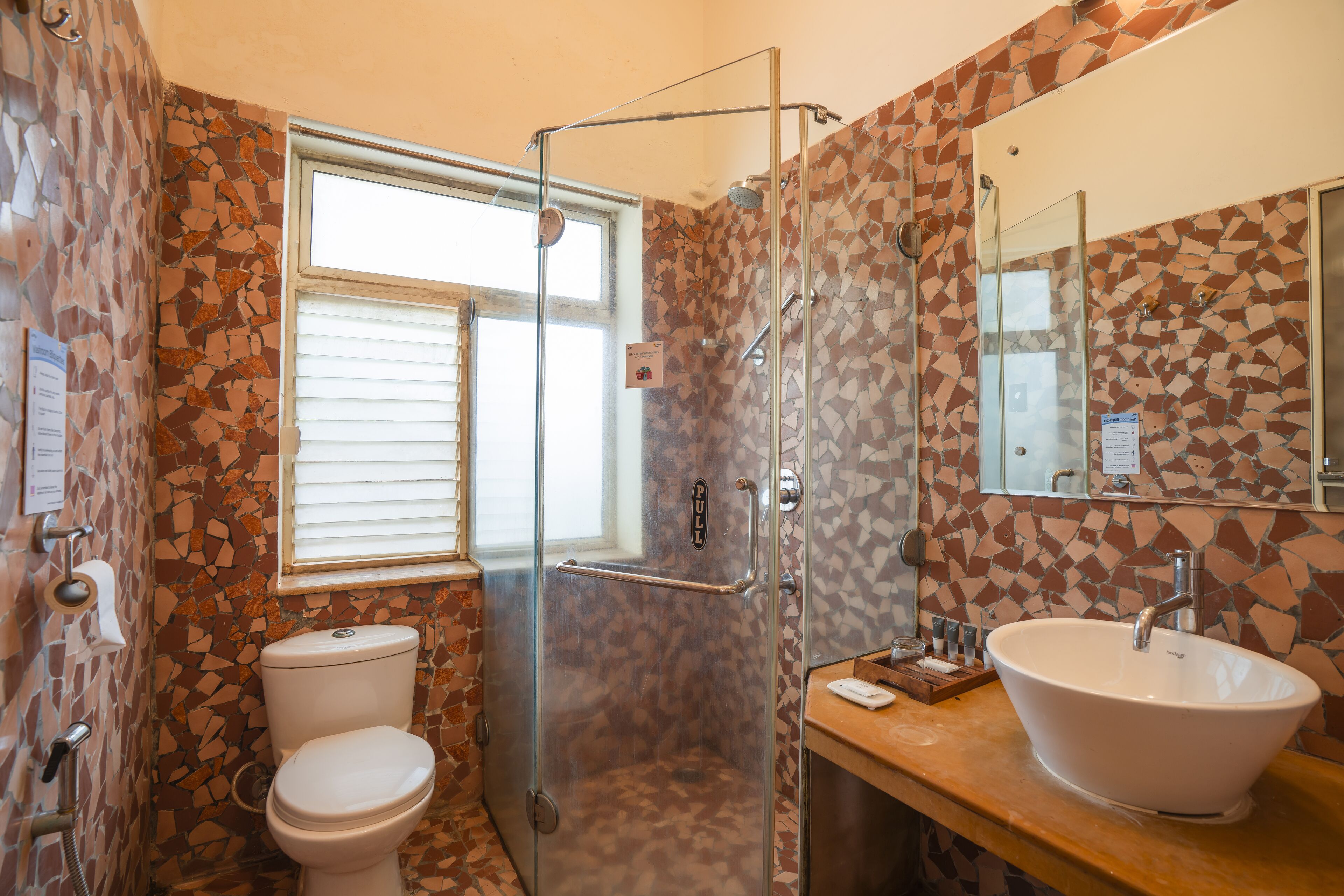 A bathroom with a mosaic tile wall, a glass shower enclosure, a white sink, and a toilet.