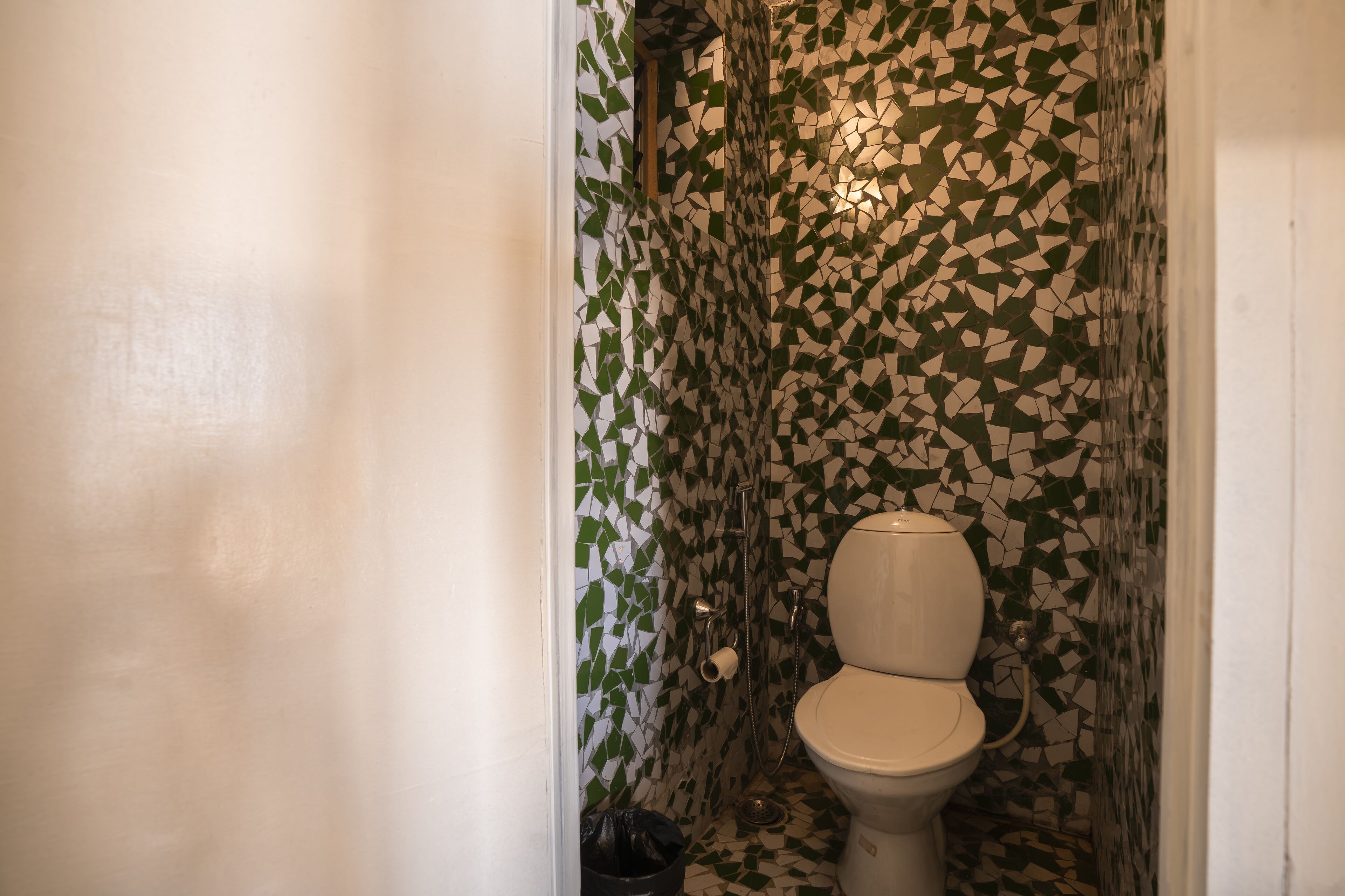 Une salle de bain avec un mur recouvert de mosaïques, des toilettes et une poubelle.