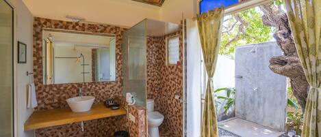 A bathroom with a tiled backsplash, a wooden vanity, a white sink, a toilet, and a shower area with a glass door.