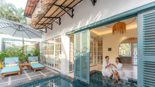 Un área de piscina con sillones de descanso y una pareja sentada junto a la piscina.