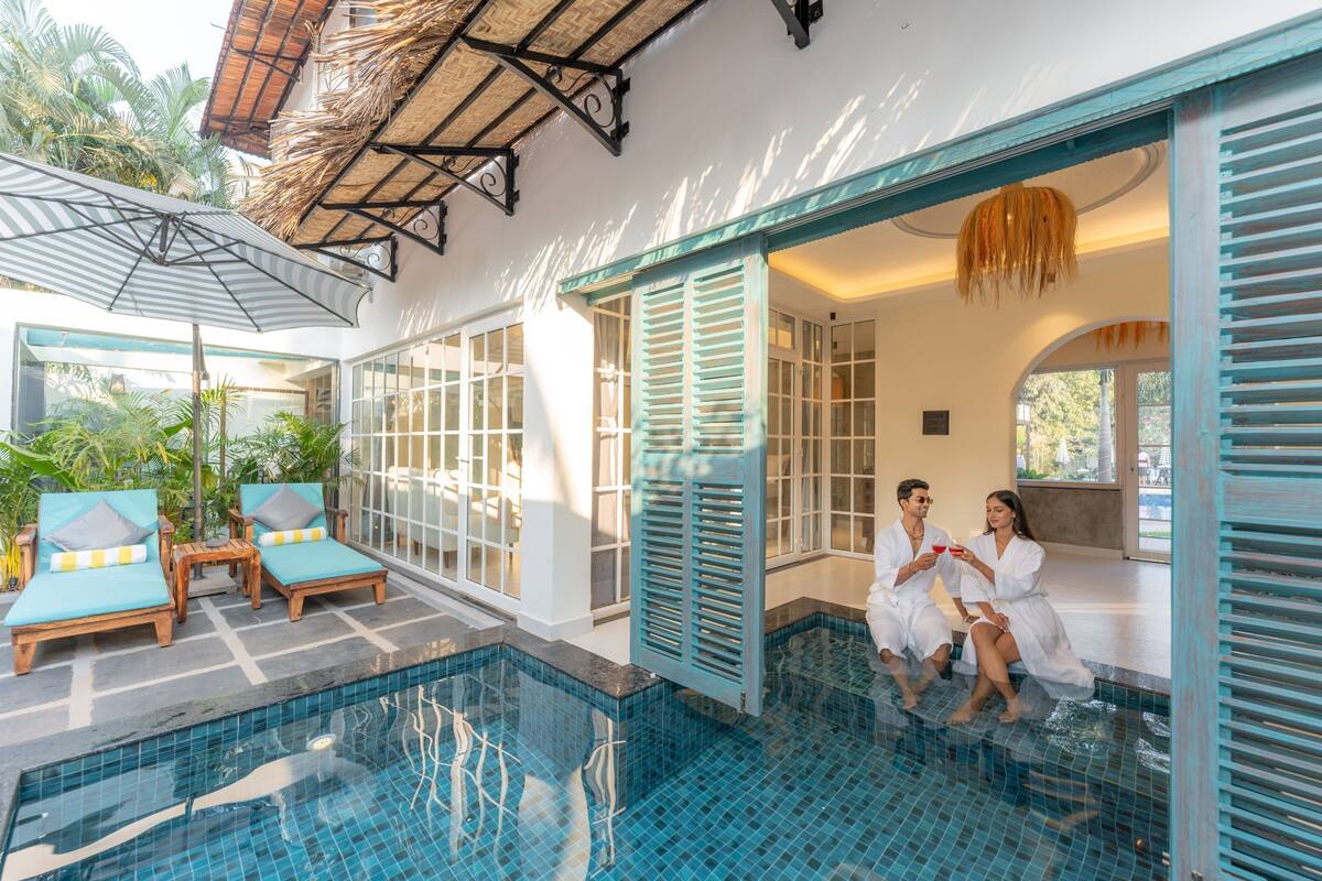 A pool area with lounge chairs and a couple sitting by the pool.